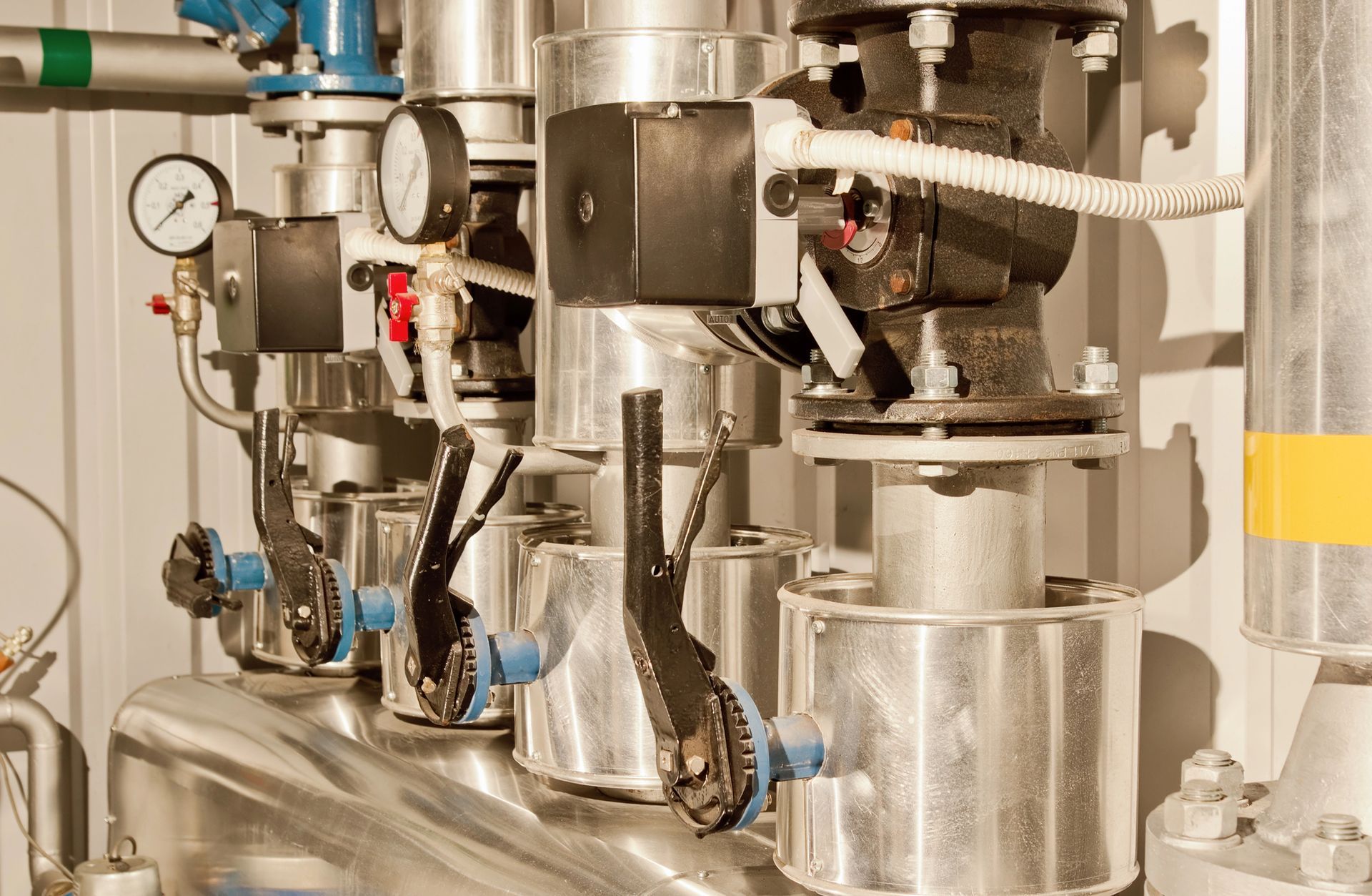 Tubi idraulici industriali con isolamento metallico, manometri e maniglie delle valvole nere in un ambiente di servizio.