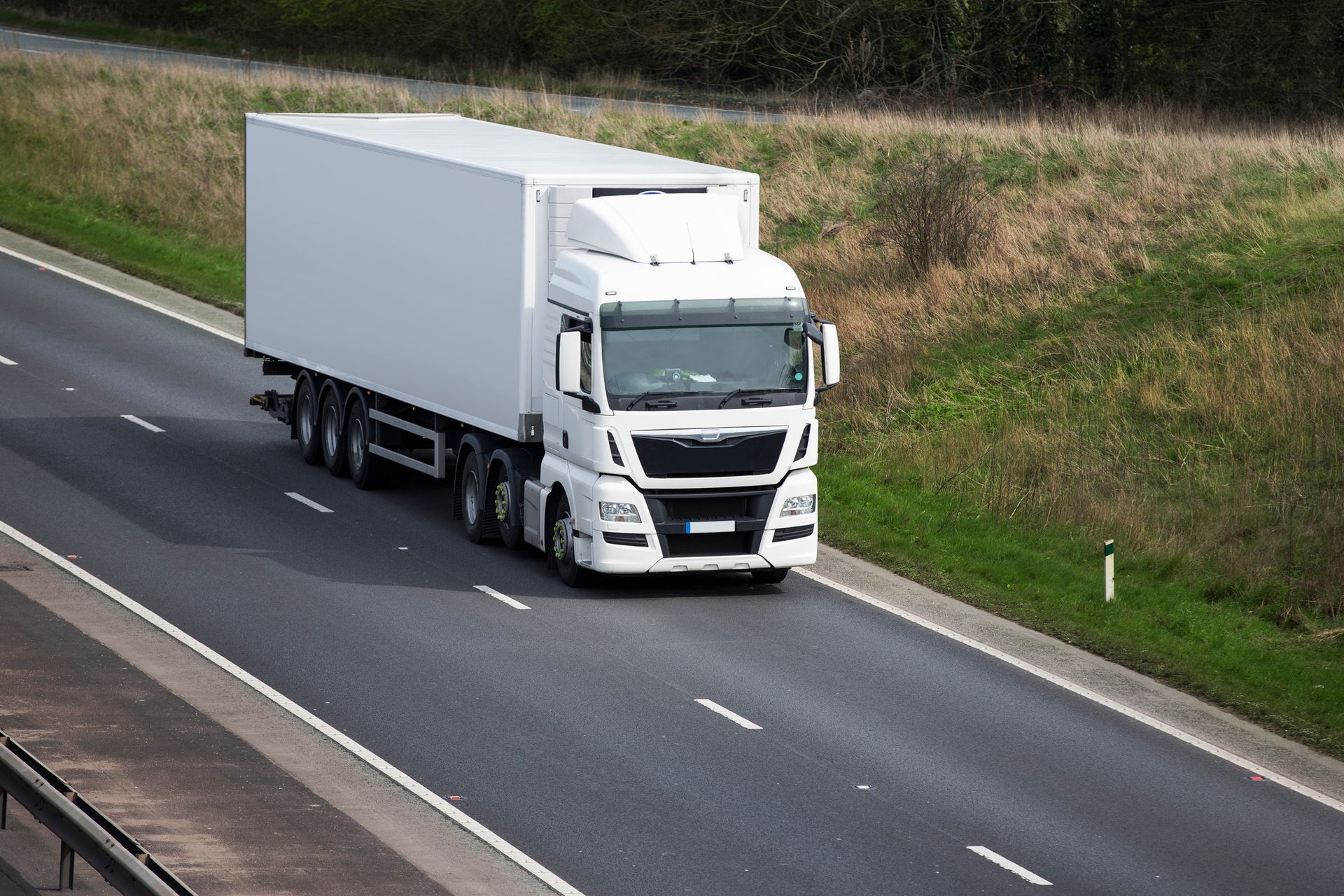 Un camion bianco percorre un'autostrada asfaltata costeggiando un ciglio erboso.