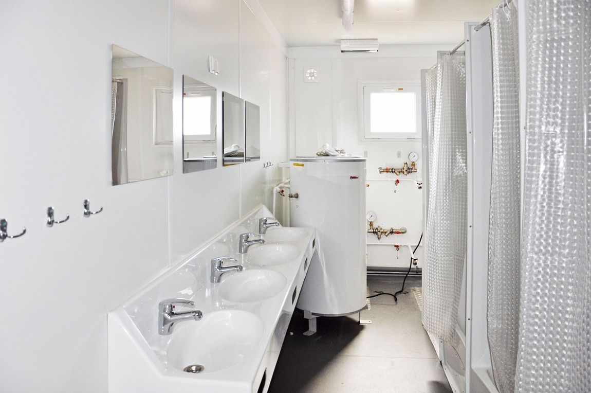 Un luminoso e sterile bagno comune con doccia e lavandino, con pareti bianche, tre lavandini e diverse cabine doccia con tenda.