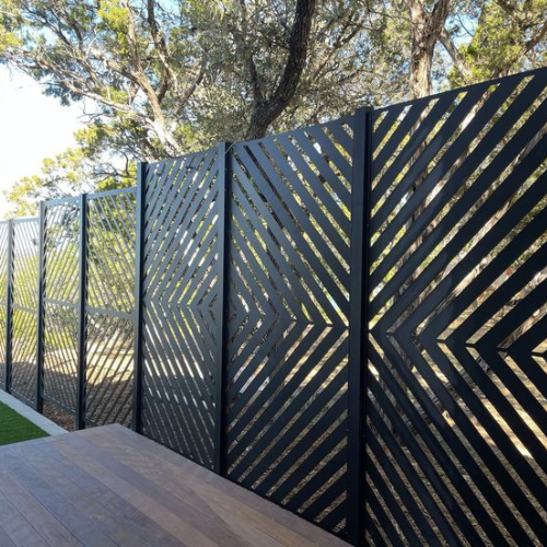 A black fence with a geometric pattern is surrounded by trees.