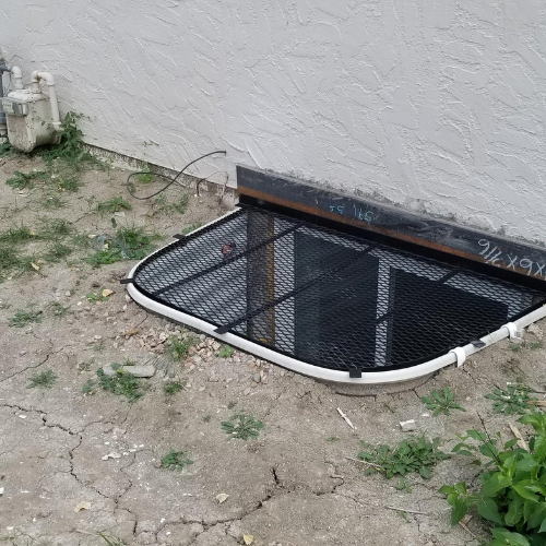 A window well with a screen on it is sitting on the ground next to a house.
