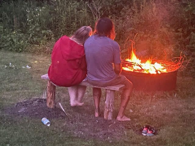 A man and a woman are sitting on a bench looking at a fire pit.