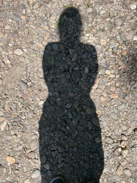 A shadow of a person standing on a gravel road