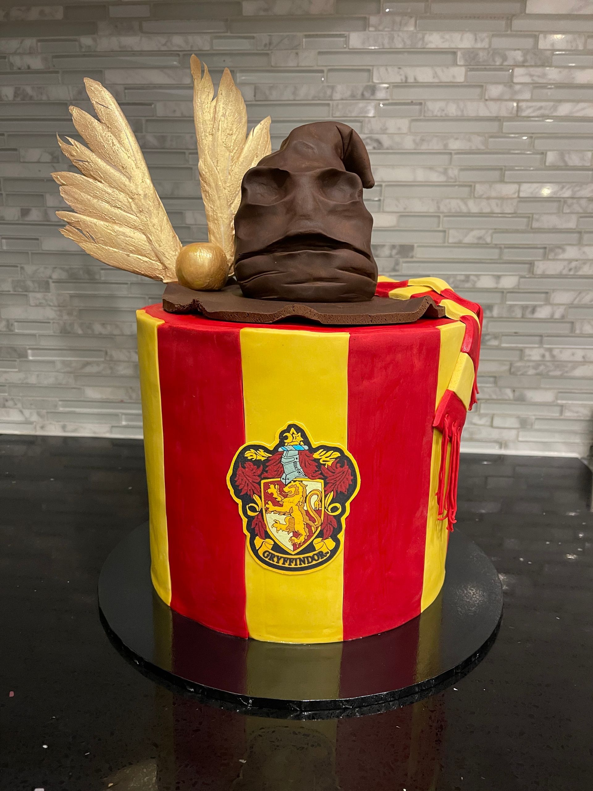 A harry potter cake with a sorting hat and golden snitch on top.