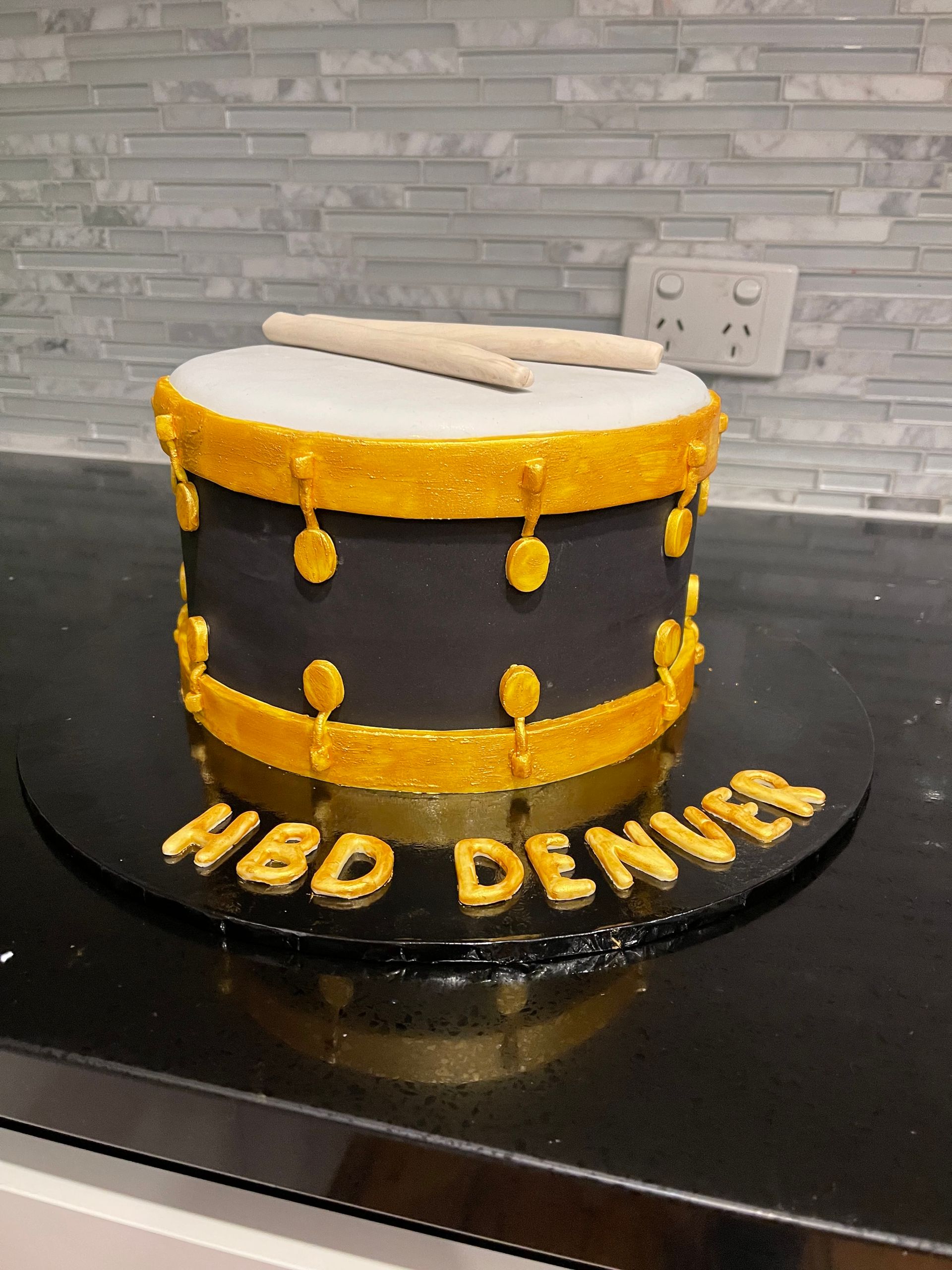 A cake that looks like a drum with the name hbd denver on it