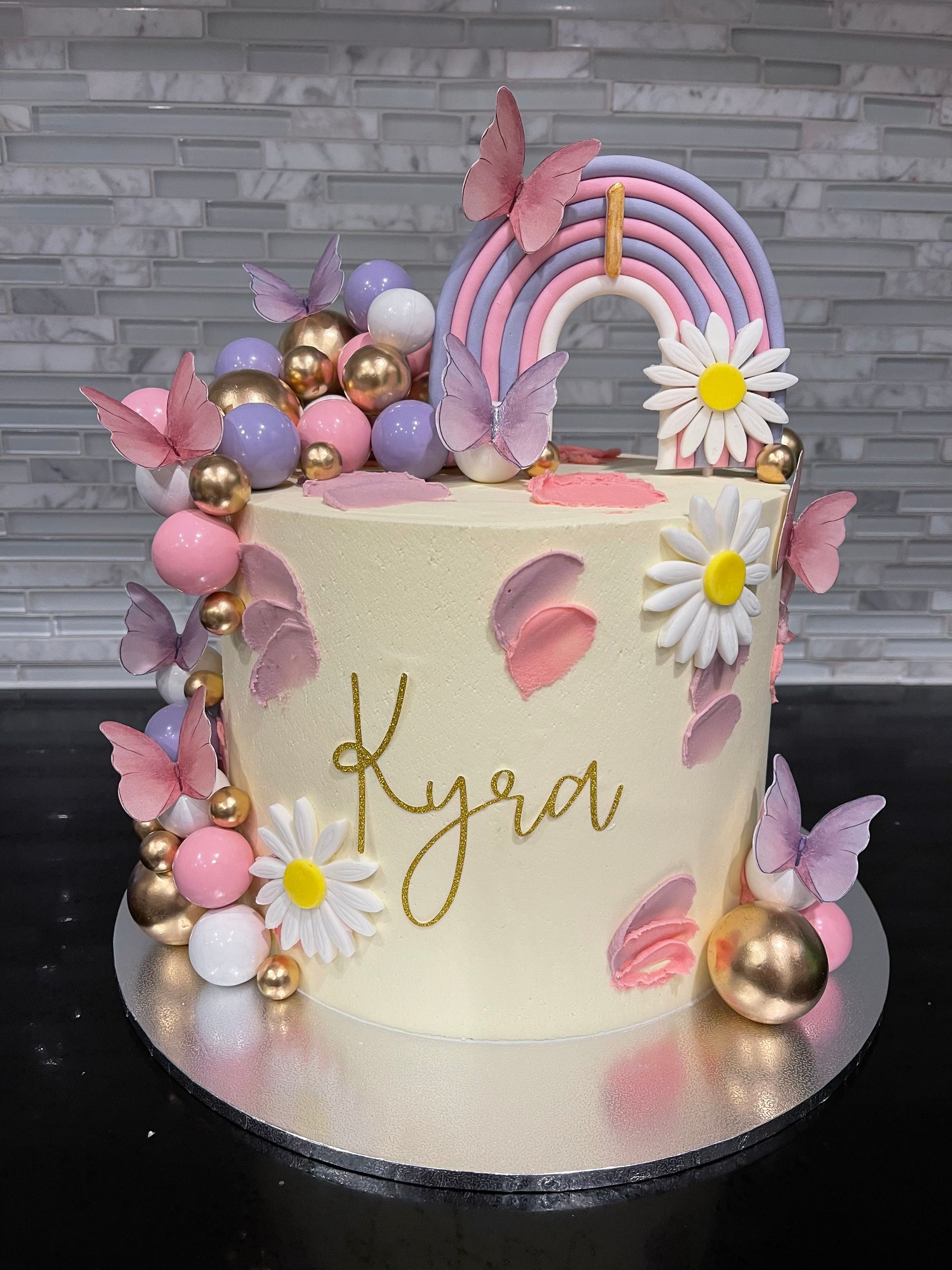 A cake with a rainbow , butterflies , daisies and balloons on it.