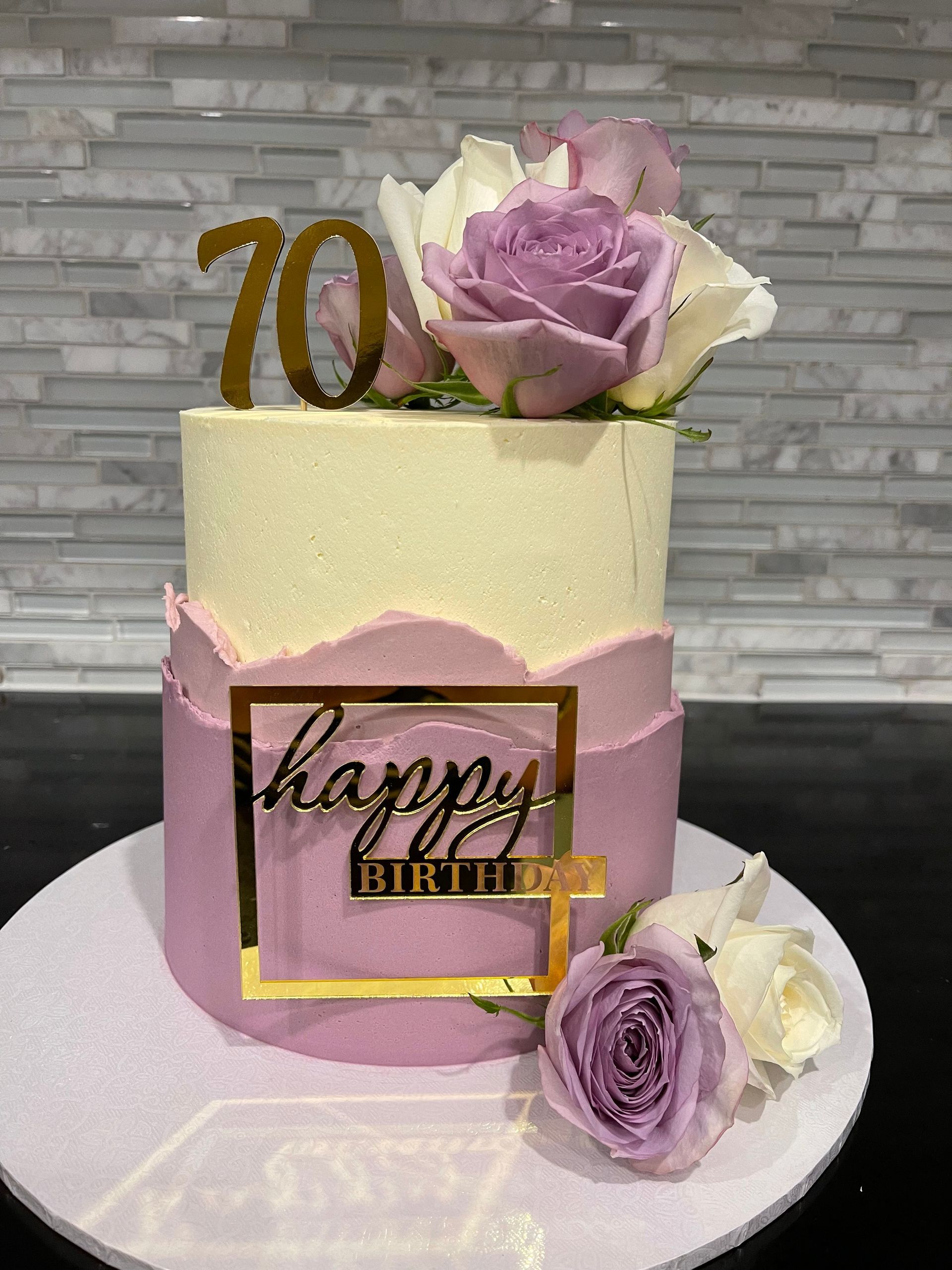 A pink and white cake with purple roses and the number 70 on top.
