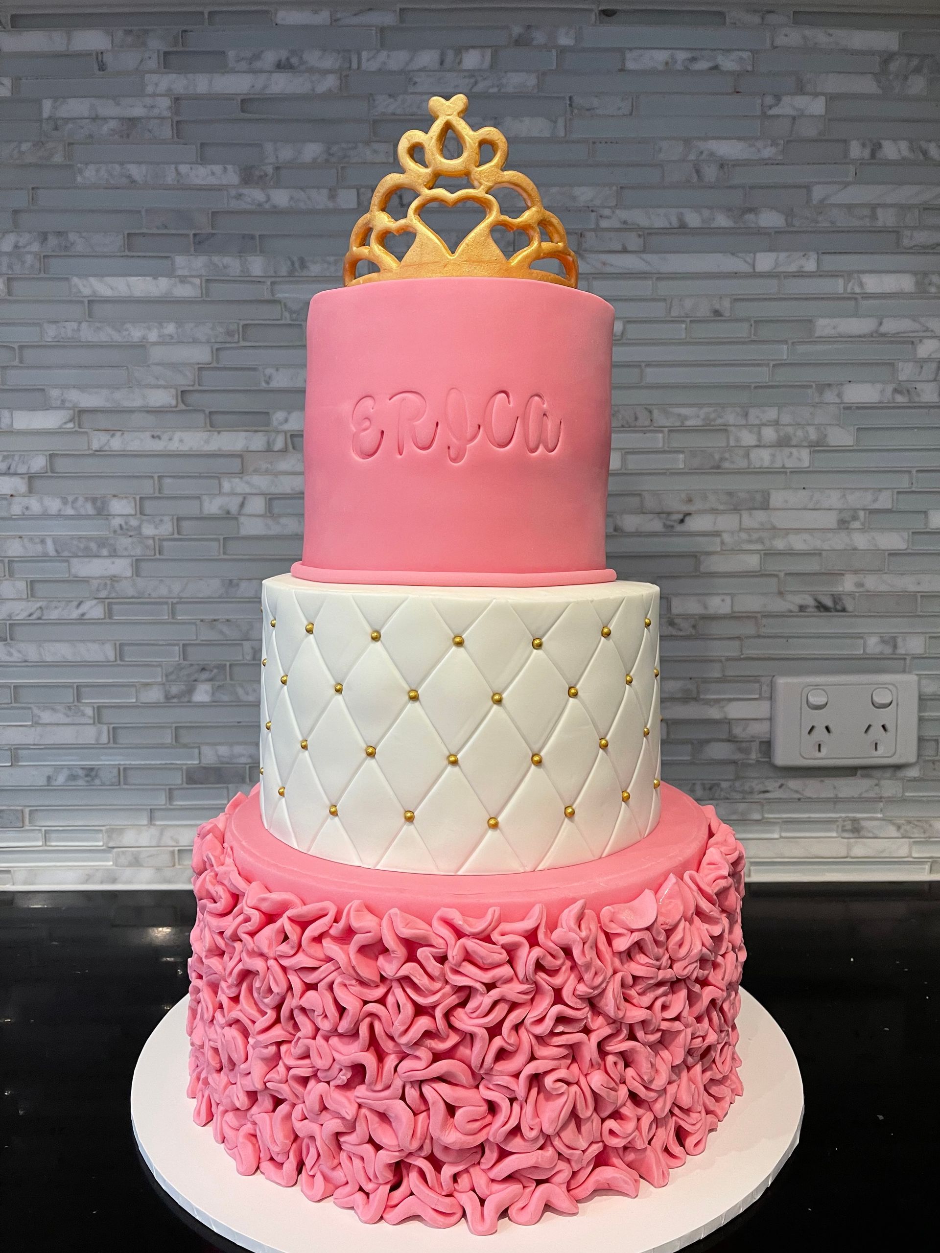 A pink and white cake with a gold tiara on top