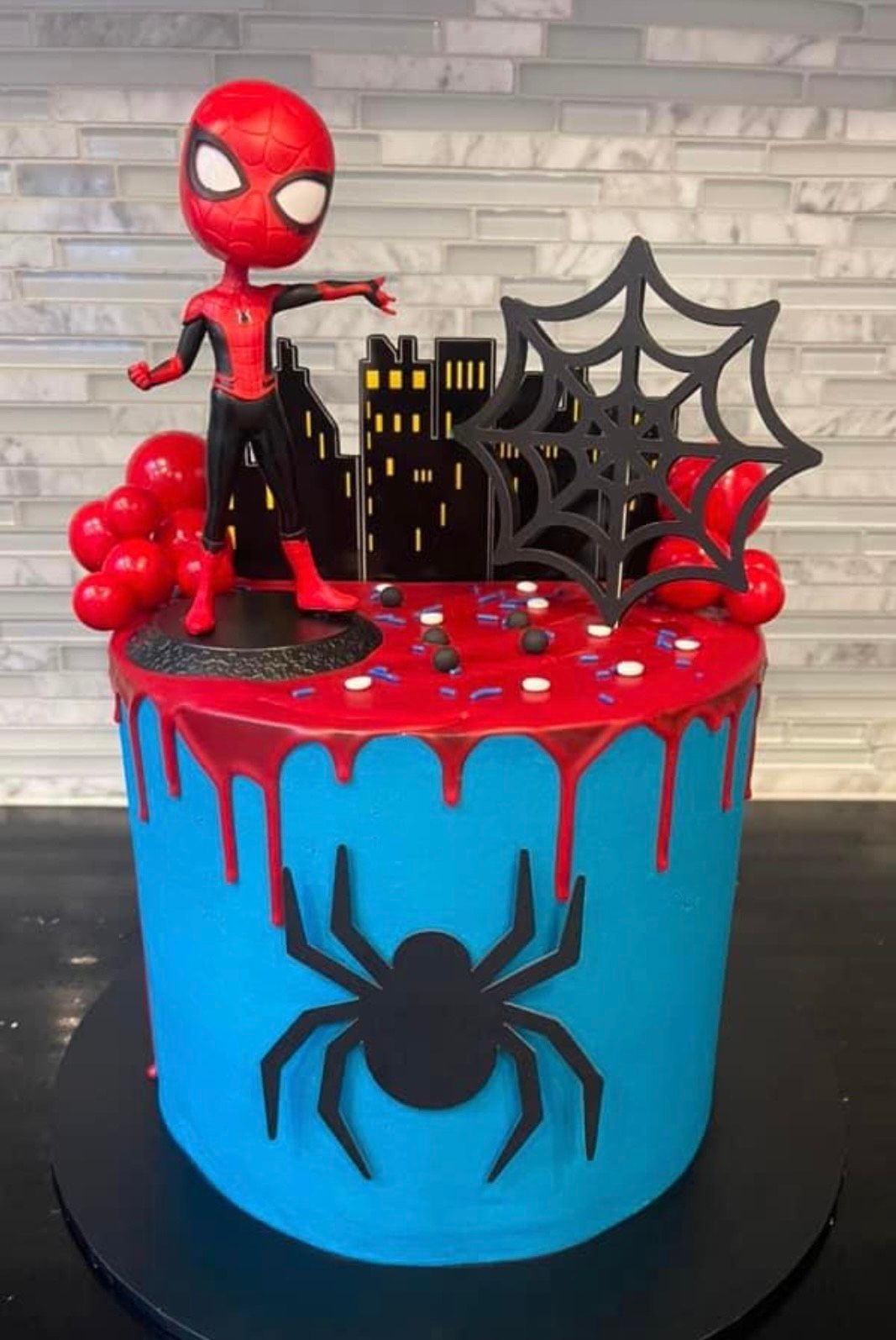 A blue and red cake with a spider man figurine on top of it.