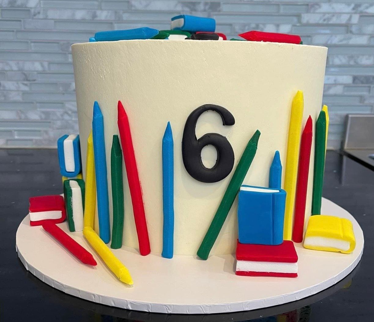A cake with pencils , books and the number six on it