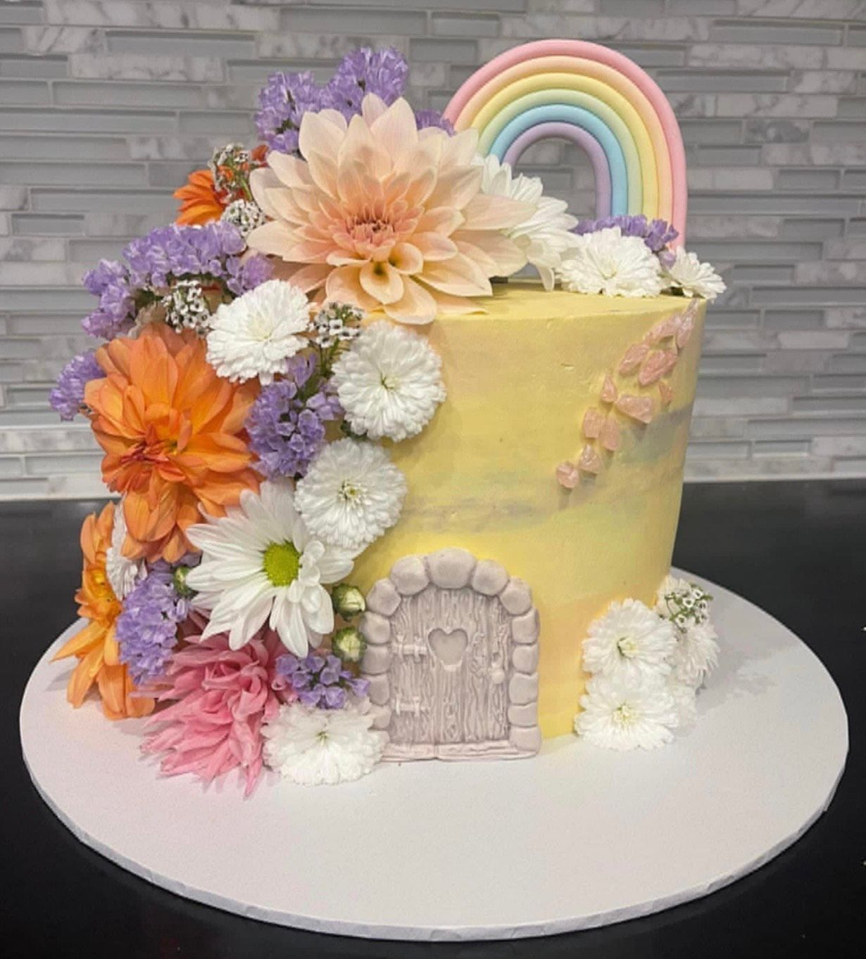 A yellow cake with flowers and a rainbow on top of it.