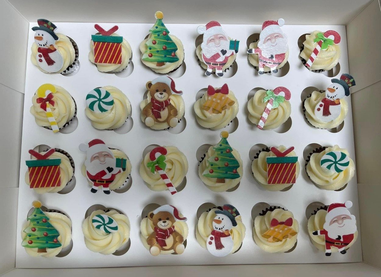 A box of christmas cupcakes with santa claus , christmas trees , and snowmen on them.