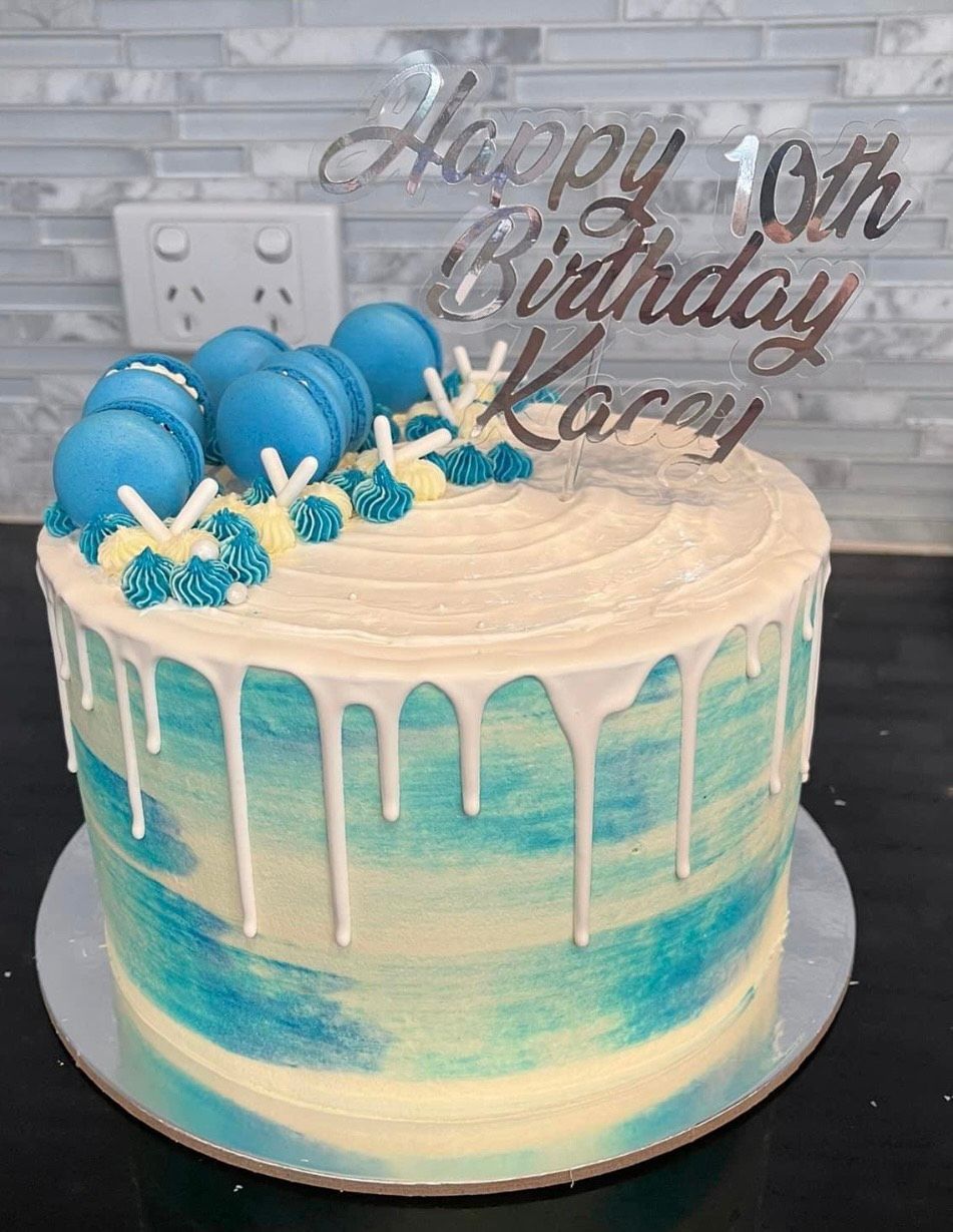 A blue and white birthday cake with macarons on top.