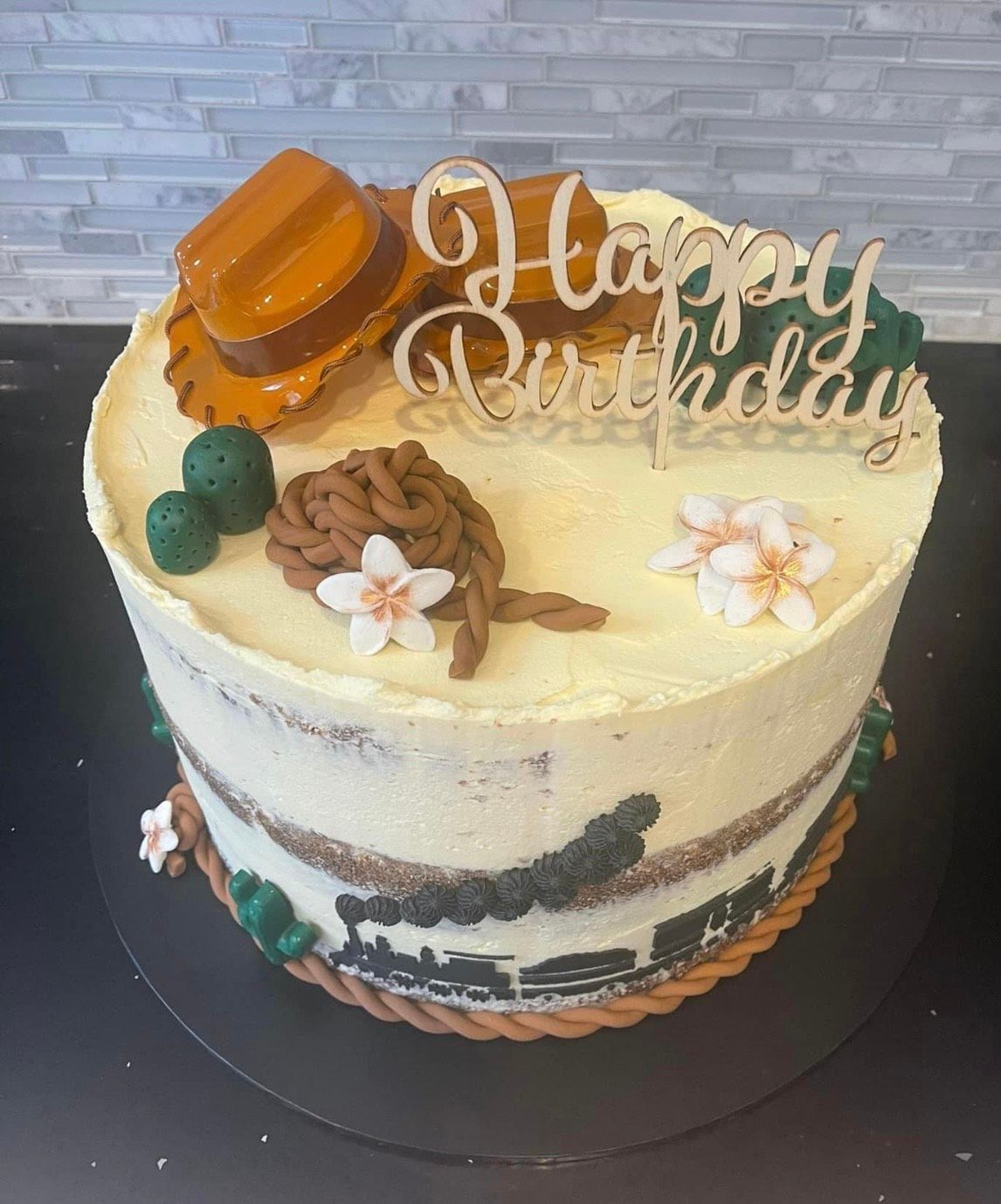 A birthday cake with a cowboy hat and flowers on it