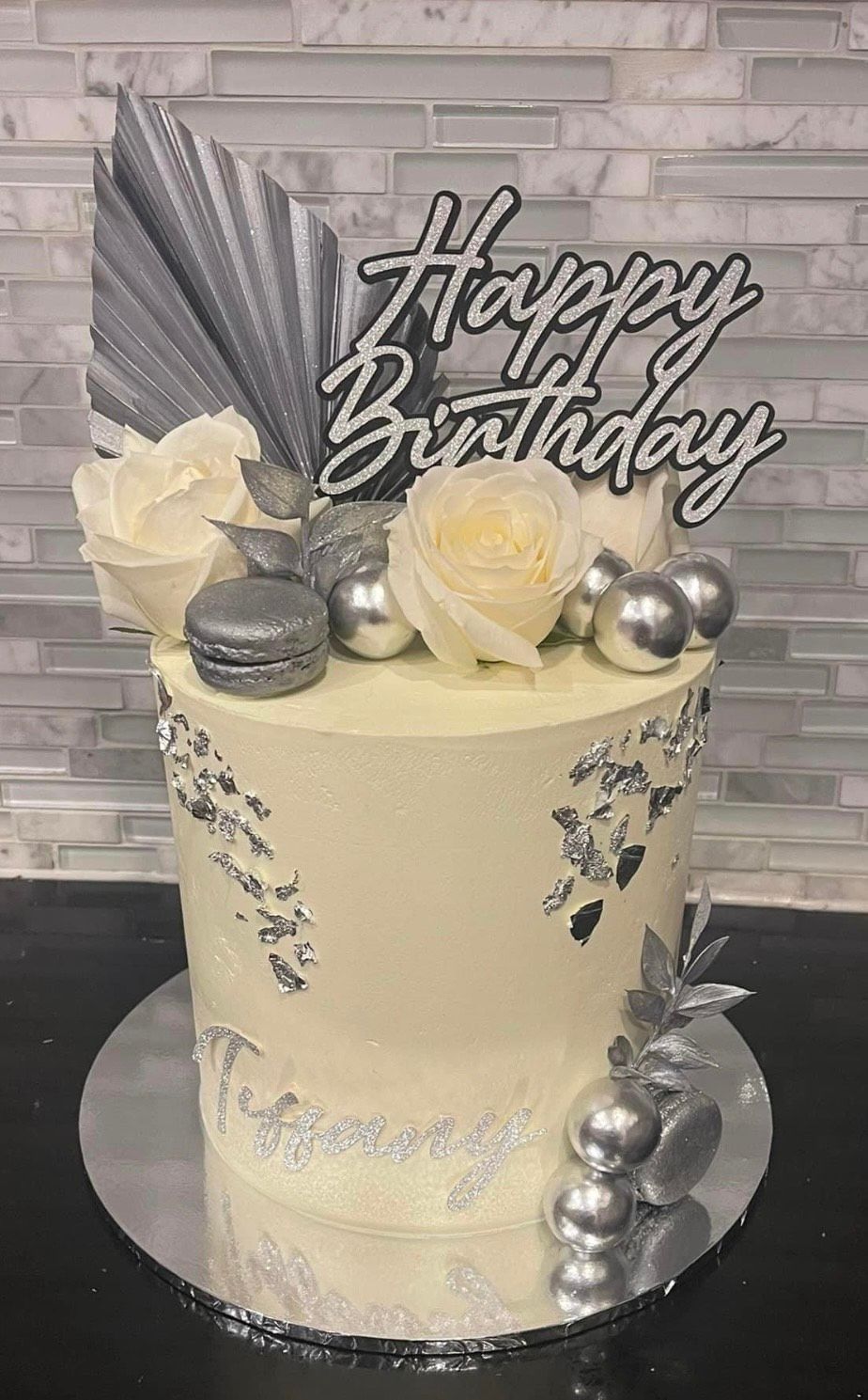 A white birthday cake with silver decorations and a happy birthday topper.