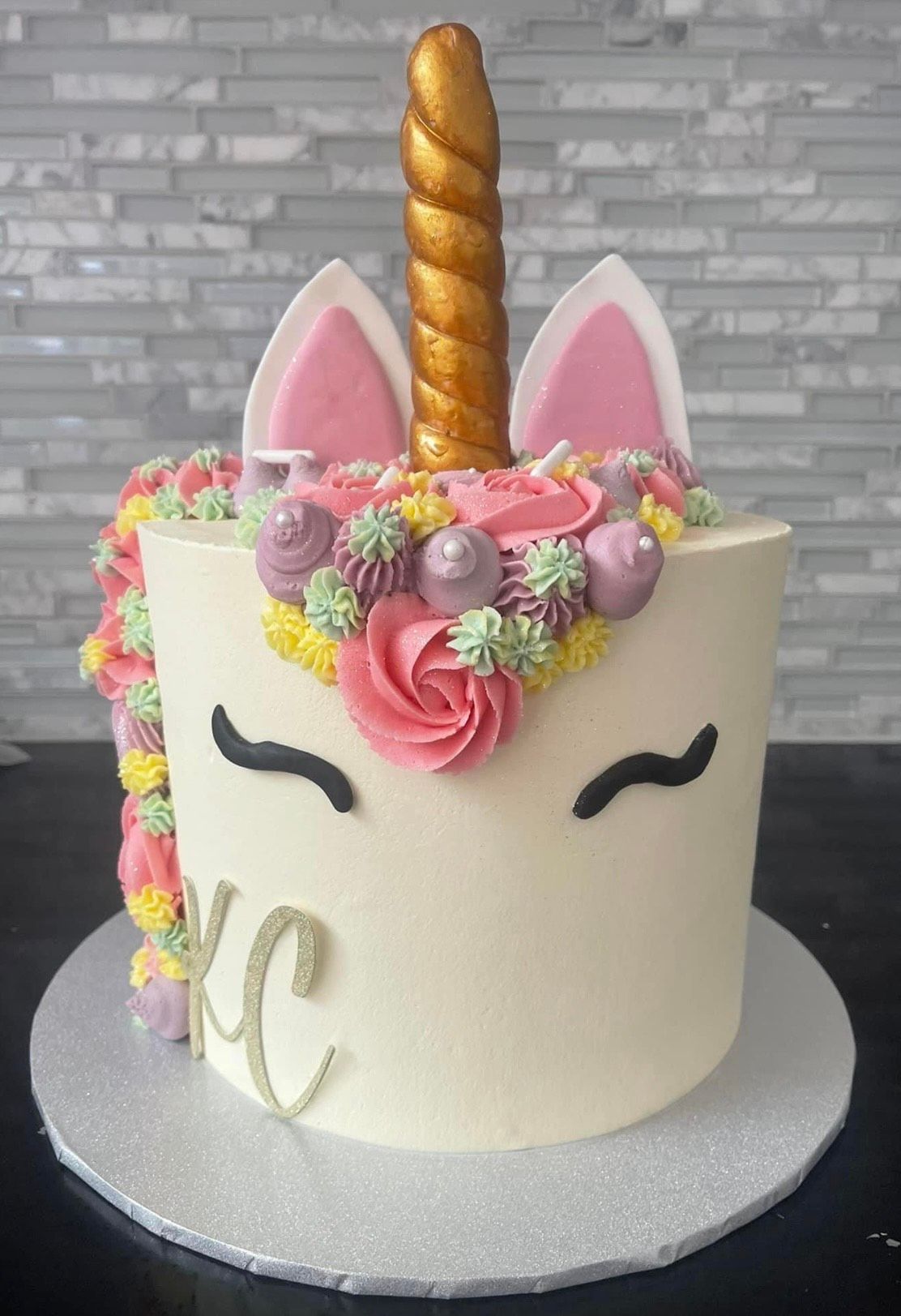 A unicorn cake with a gold horn and ears is on a table.