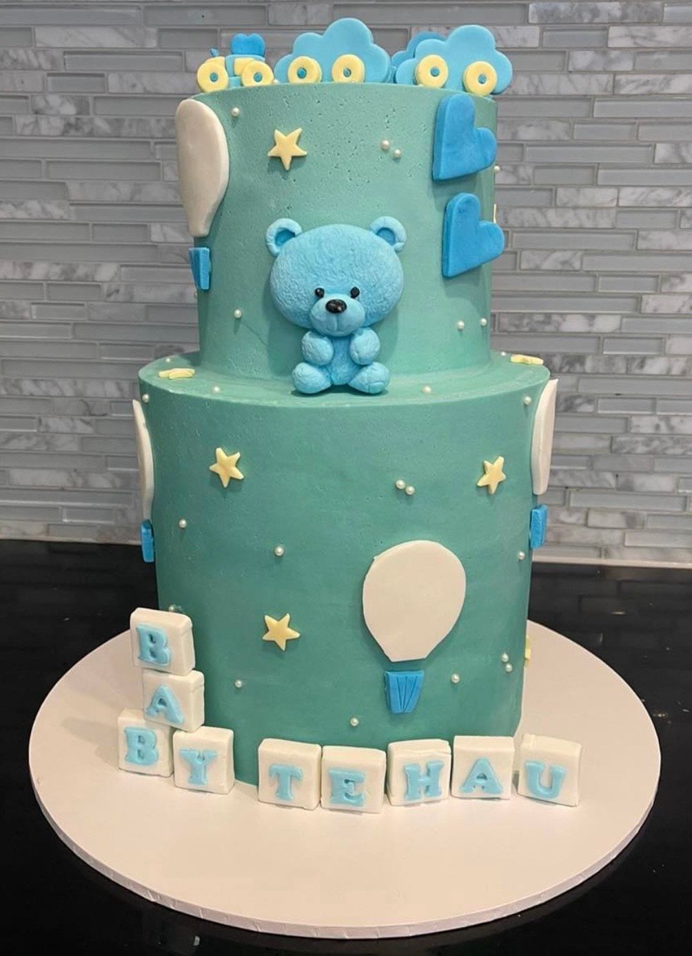 A baby shower cake for a boy with a teddy bear on top.