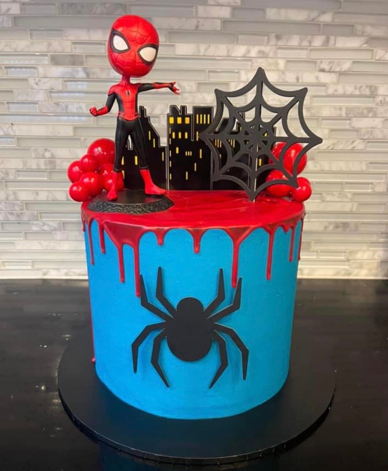 A blue and red cake with a spider man figurine on top of it.
