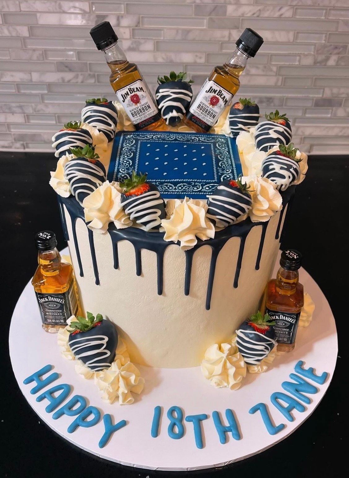 A birthday cake with strawberries and bottles of alcohol on top.