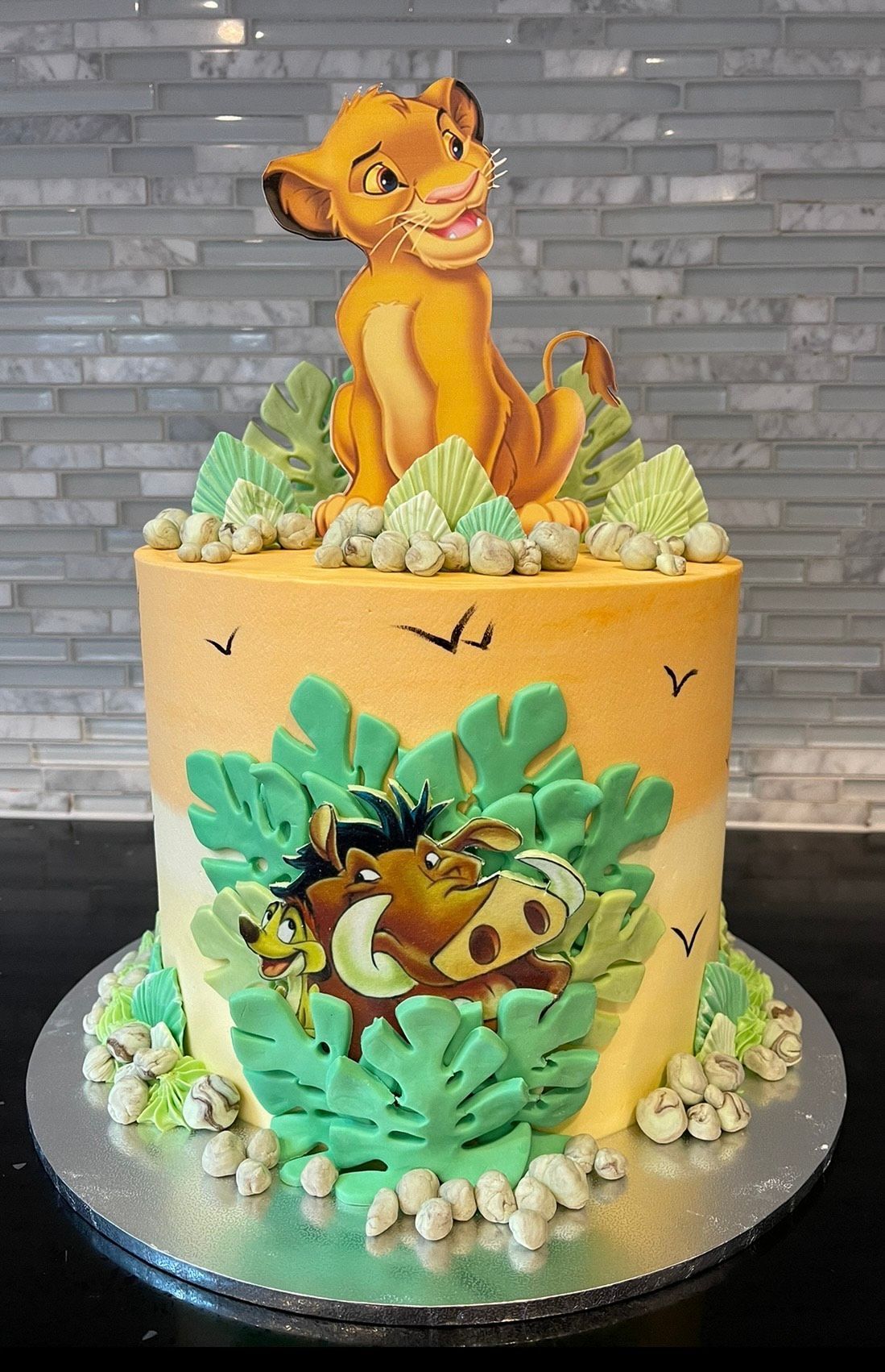 A lion king cake with simba , timon , and pumba on it.