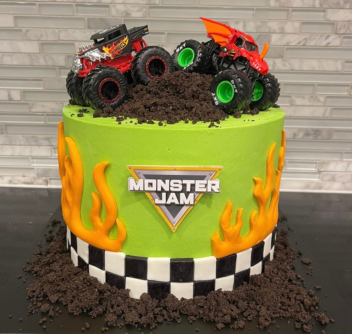 A monster jam cake with two monster trucks on top of it.