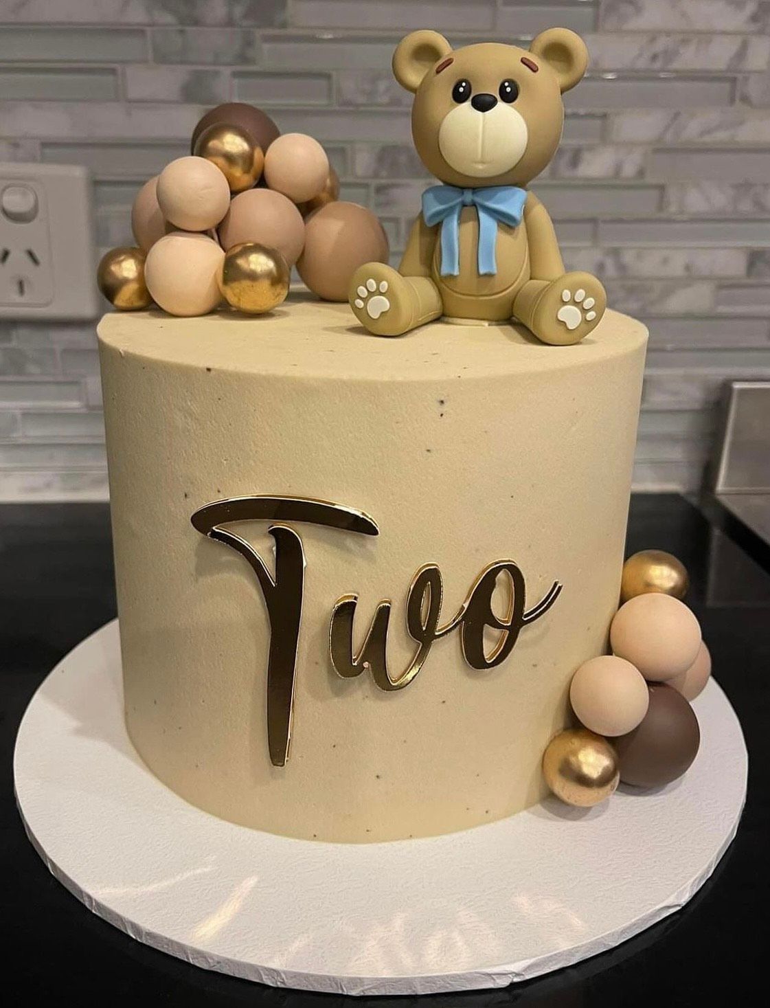 A cake with a teddy bear on top that says two