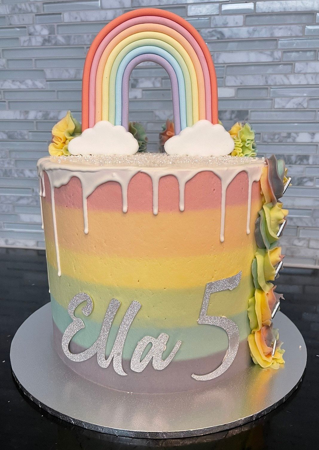 A colorful birthday cake with a rainbow and clouds on top.