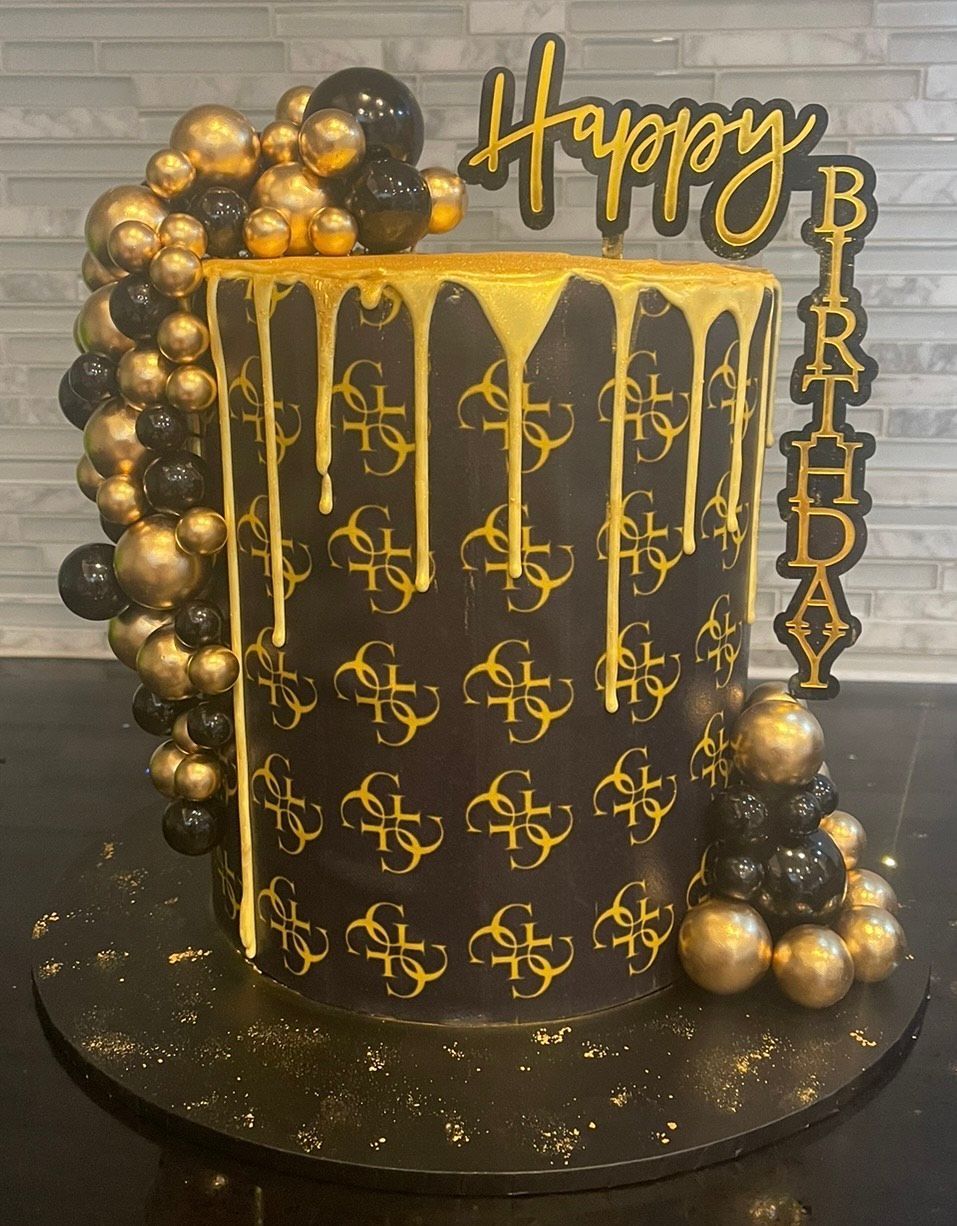 A black and gold birthday cake with a happy birthday topper