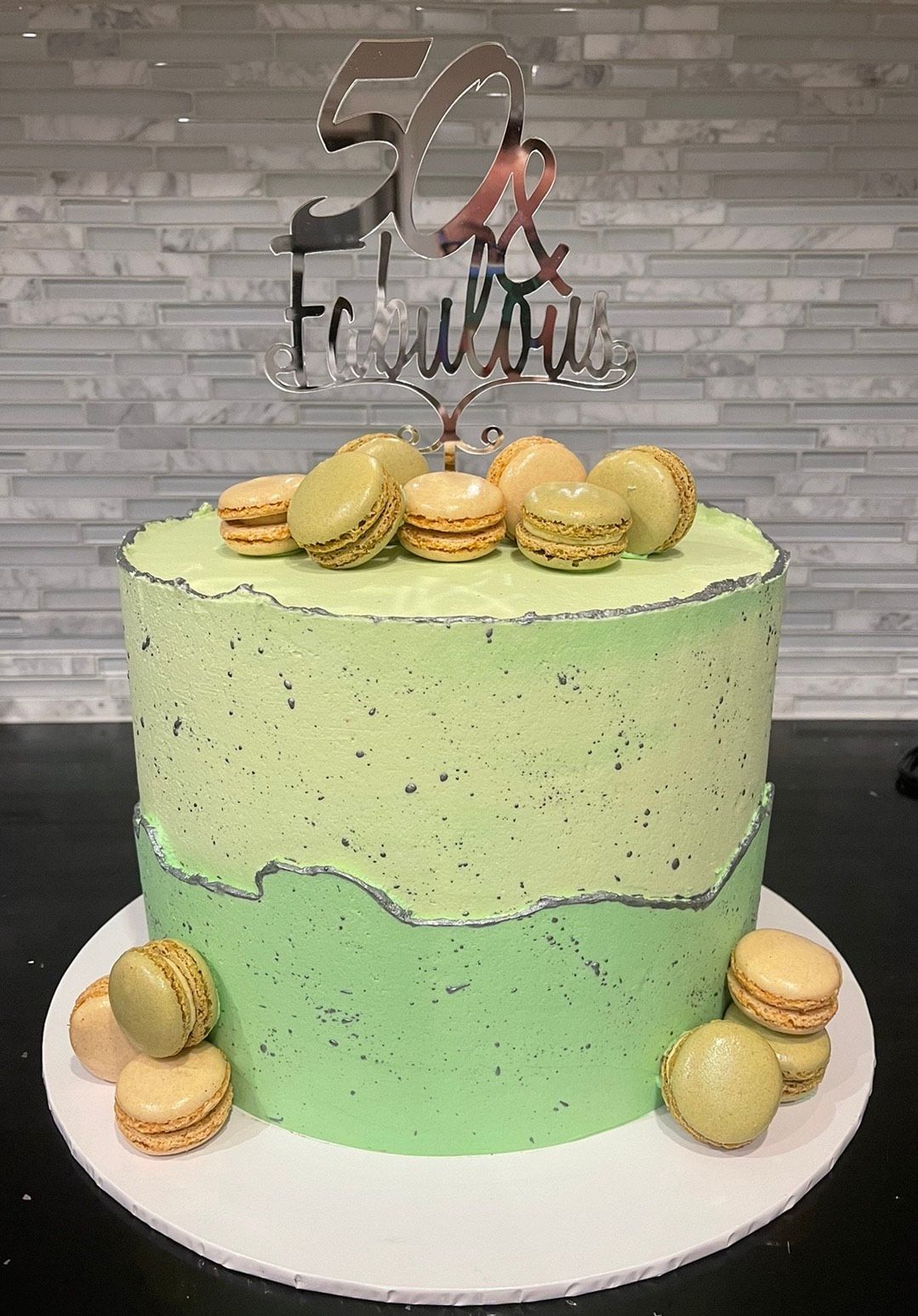 A green cake with macarons on top is on a plate.