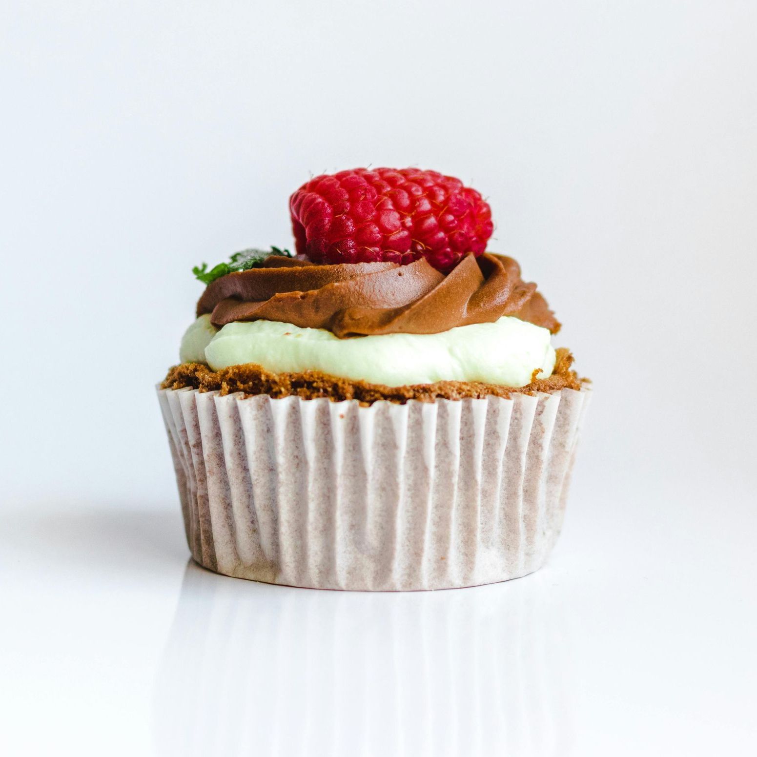 A cupcake with chocolate frosting and a raspberry on top