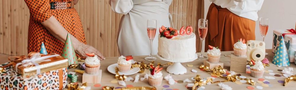 A group of women are standing around a table with a cake and cupcakes.