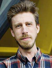 A man with a beard is wearing a plaid shirt and looking at the camera.