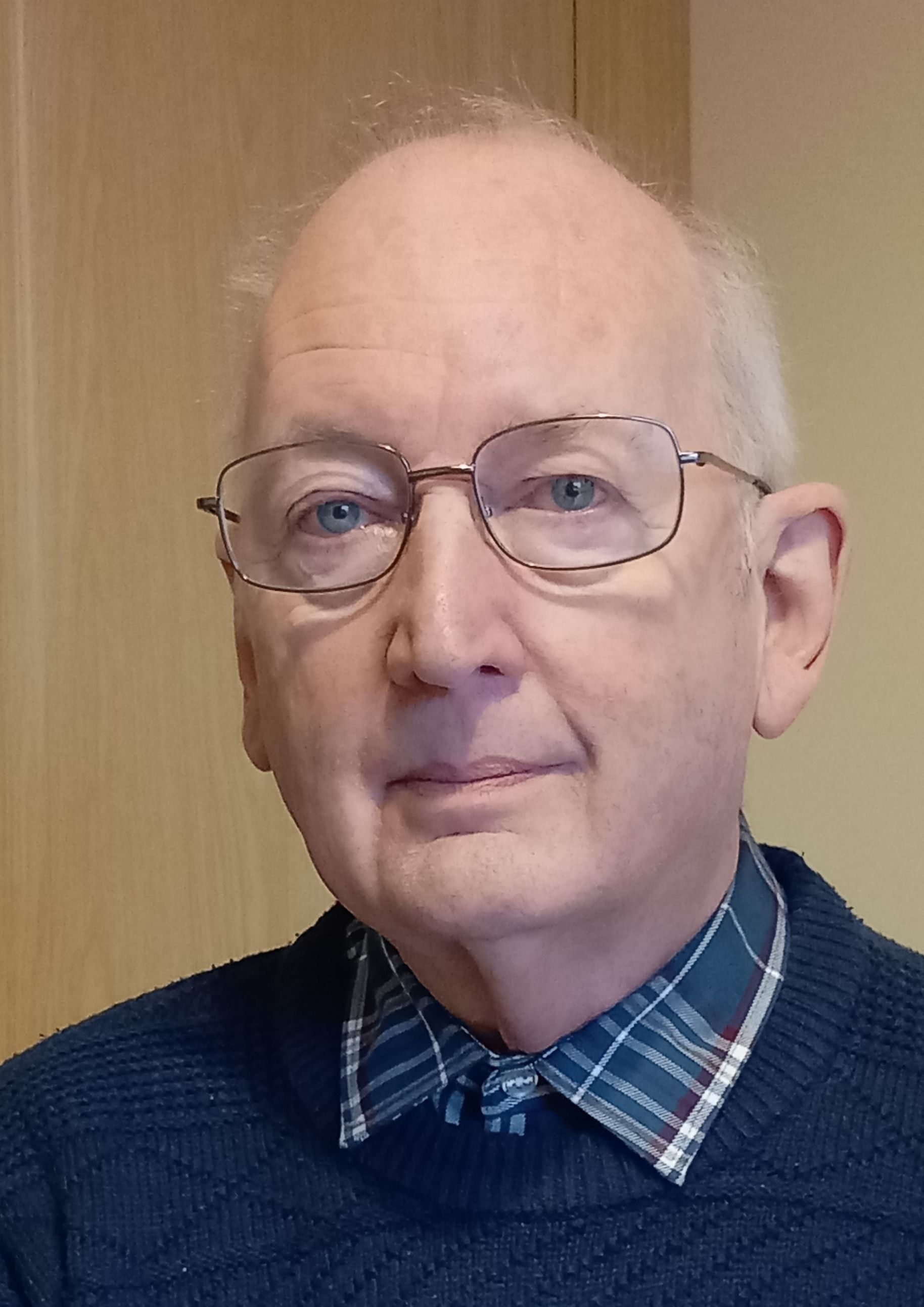 A man wearing glasses and a plaid shirt is looking at the camera.