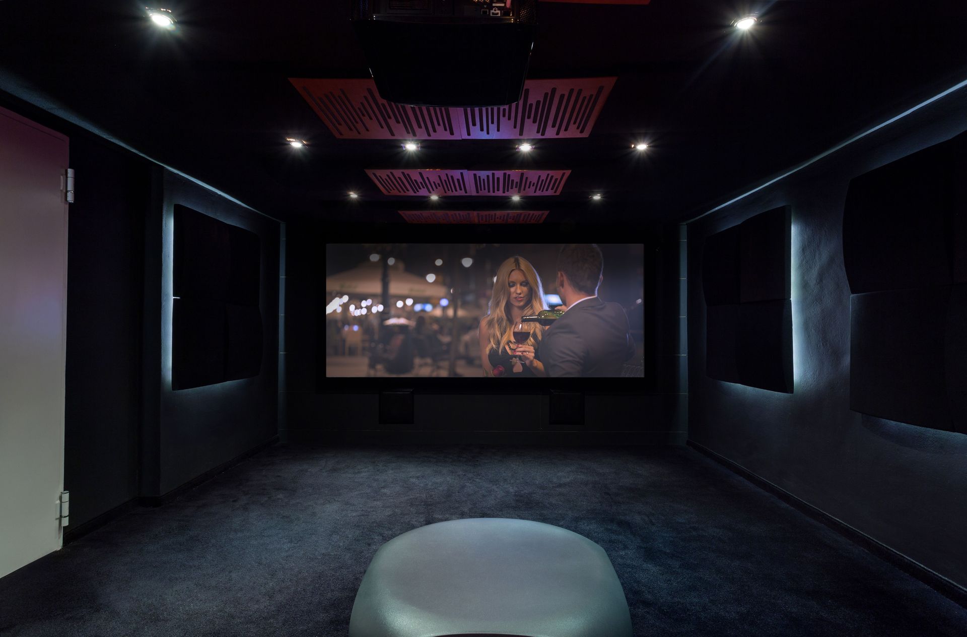 Dark home theater with large screen, sound panels, projector, and gray seating.