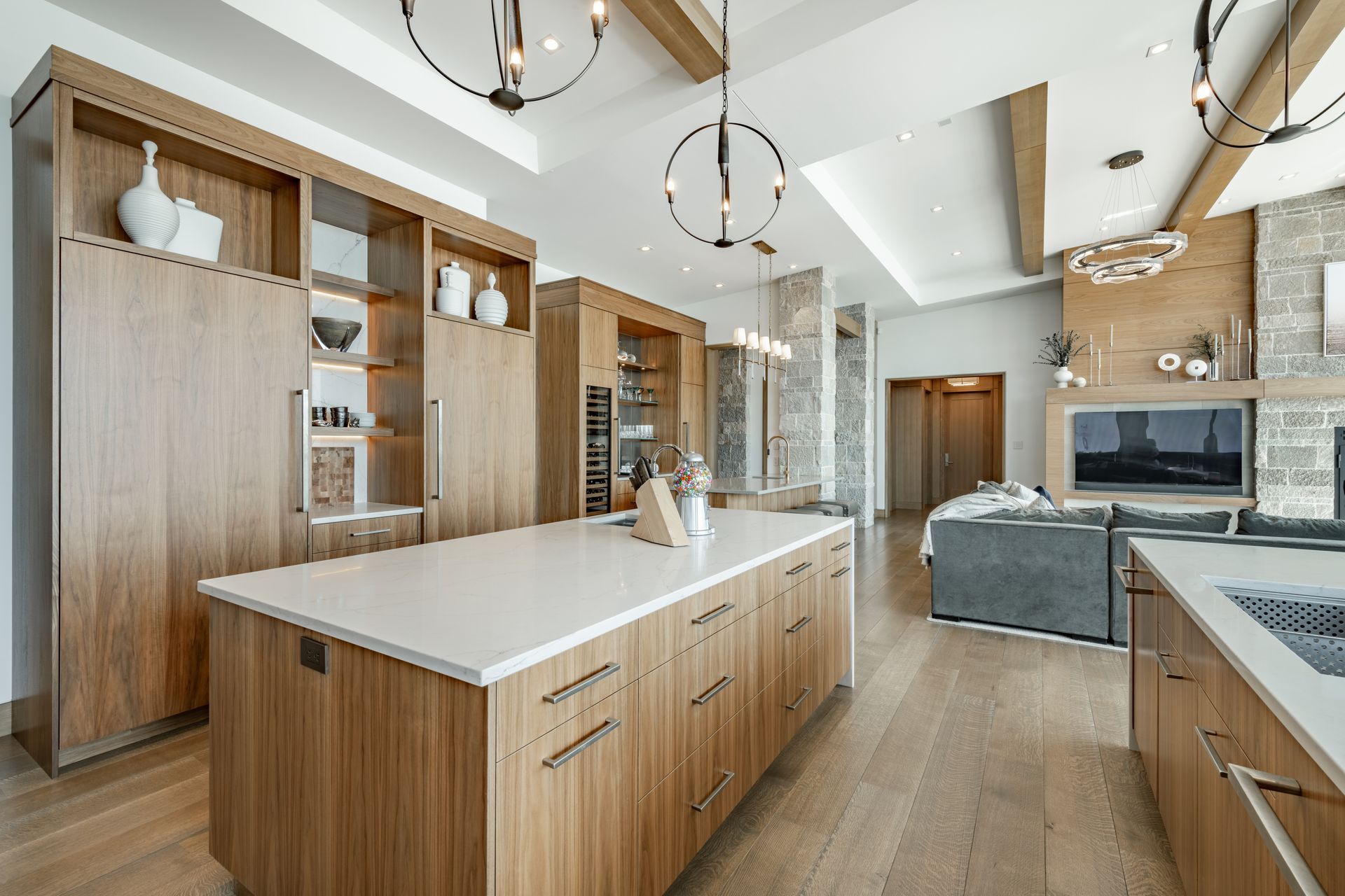 Modern kitchen with wood cabinetry, island, and stone fireplace in the background.