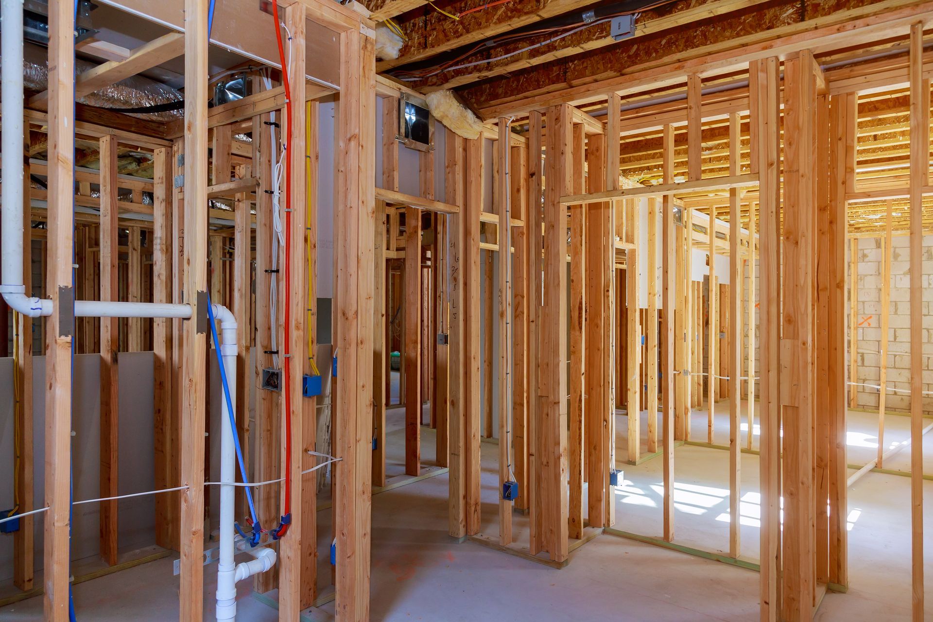 Interior view of a building under construction, showing wooden wall framing, plumbing pipes, and exposed electrical wiring.