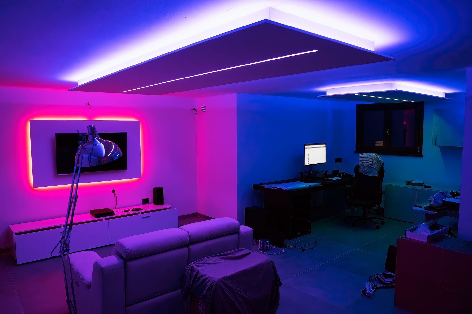 A room with pink and blue LED lighting; a TV, desk, and couch are visible.