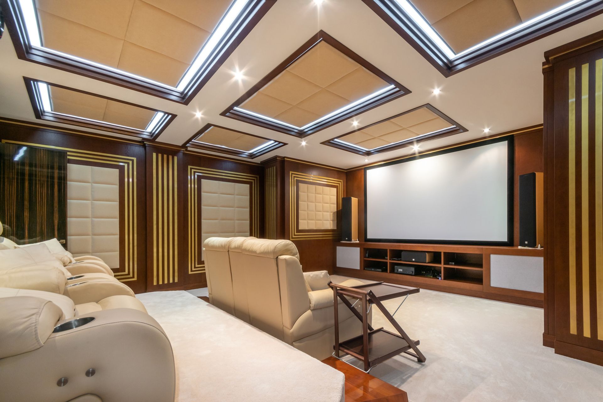 Home theater with cream-colored seating, a large screen, and wooden paneling with recessed lighting.