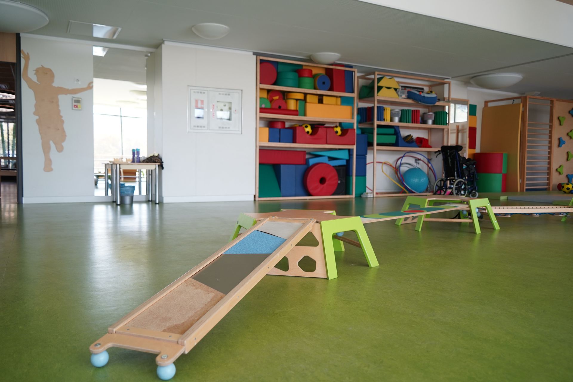 Indoor play area with colorful blocks, balance beams, and green floor.