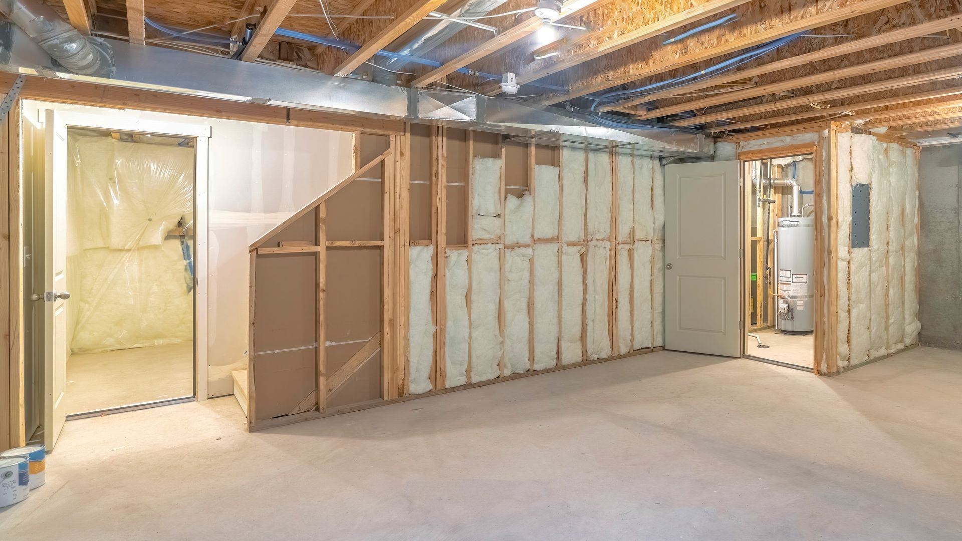 Basement interior under construction, wood framing with insulation, open doorways, and concrete floor.
