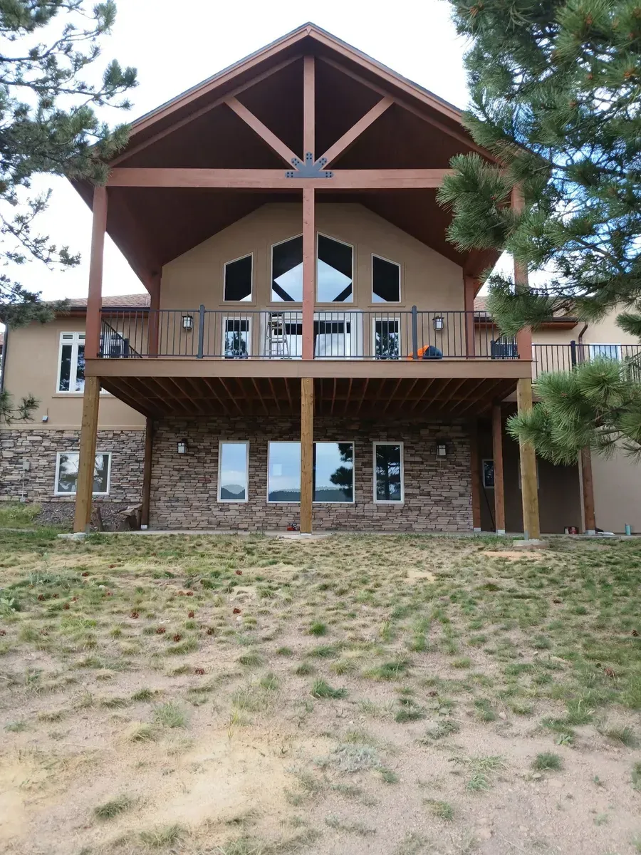 Two-story house with a wooden deck and gabled roof, tan stucco siding, and stone foundation.