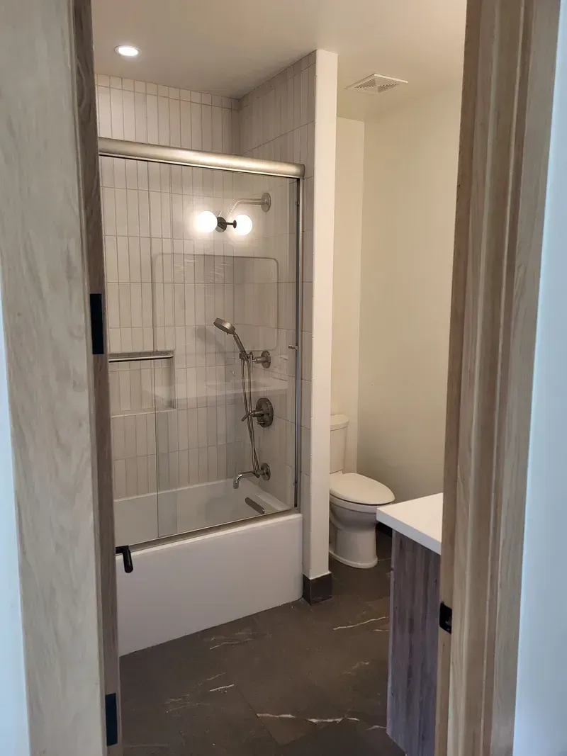 Bathroom interior with a shower/tub, toilet, and vanity visible through a doorway.