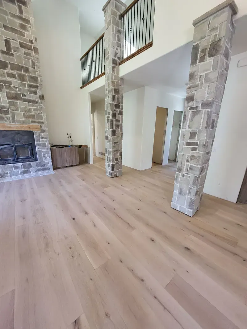 Light wood flooring in a large room with stone pillars and a fireplace.