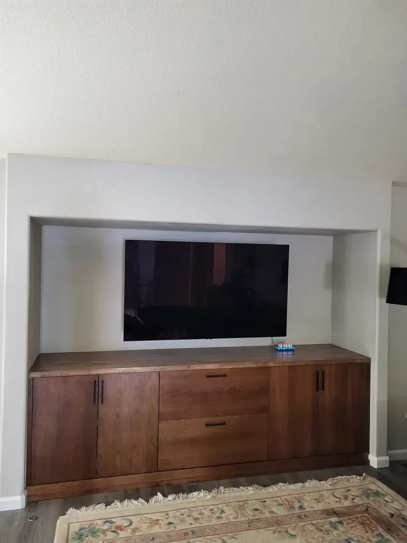 Built-in wooden entertainment center with TV mounted above it, set into a neutral-colored recessed wall.