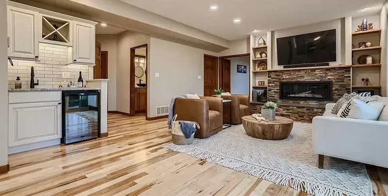 Spacious living room with bar, fireplace, and built-in shelving; light wood floors, neutral tones.
