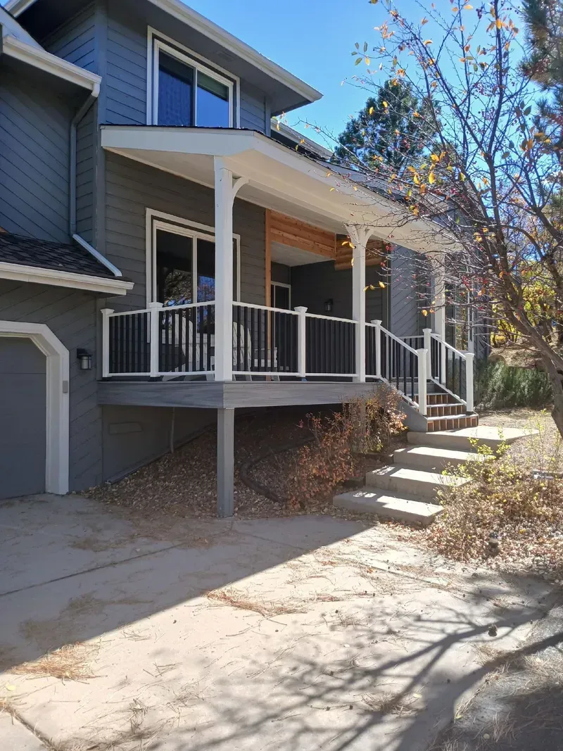 Two-story house with a covered deck, stairs, and a garage on a sunny day.