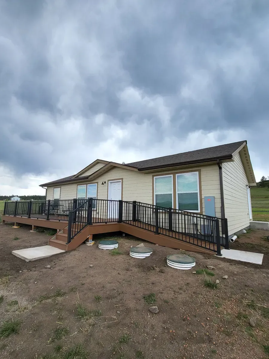 Beige house with a wooden deck and a ramp, under a cloudy sky.
