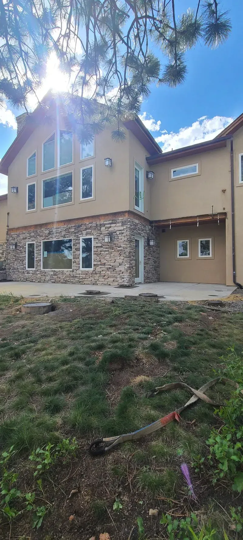 Exterior of a house with stone and tan siding, large windows, and a grassy yard.
