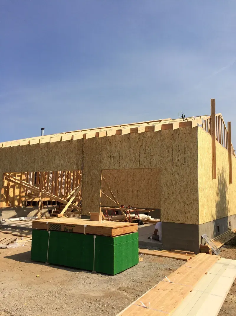Construction site: wooden frame of a building with OSB sheathing under a clear sky.
