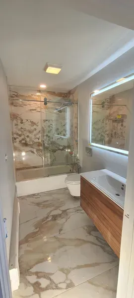 Modern bathroom with marble floors and walls, a wood vanity, and a backlit mirror.